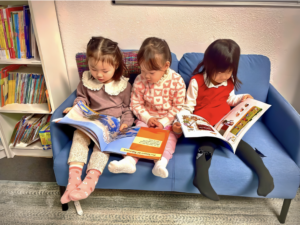 Three children sit on a blue couch while reading books.
